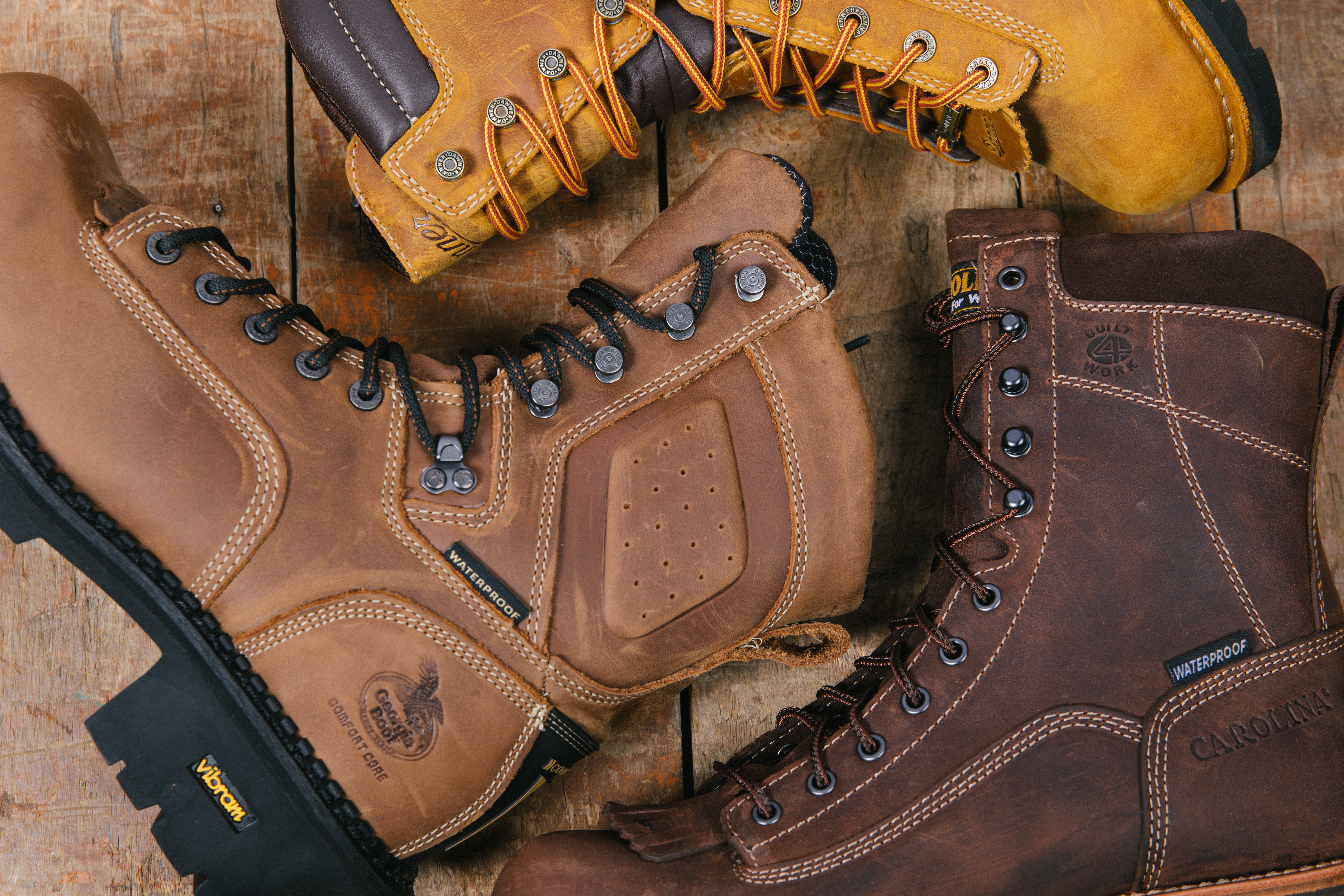 Three pairs of boots scattered in a circular position. Boot brands include Carolina Shoe, Georgia Boot and Danner. 